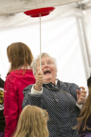 Old lady has a face of shear joy as she finally spins a red plate upon the stick during a circus workshop