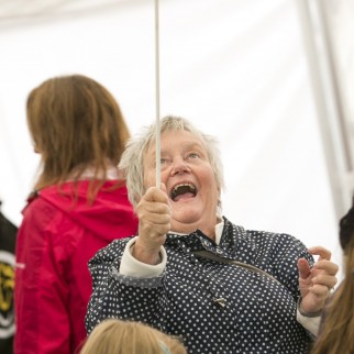 Old lady has a face of shear joy as she finally spins a red plate upon the stick during a circus workshop