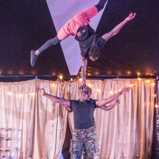 An acrobat does a one-armed handstand on top of another acrobat's head